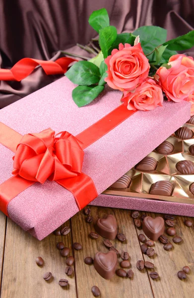 Delicious chocolates in box with flowers on table on brown background