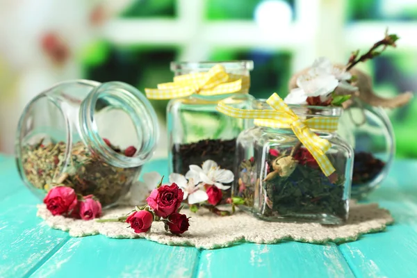 Assortment of herbs and tea in glass jars on wooden table, on bright background