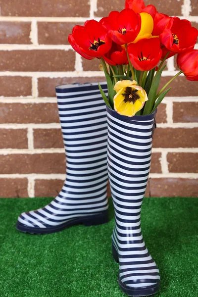 Composition of colorful tulips in rain boots on bright background