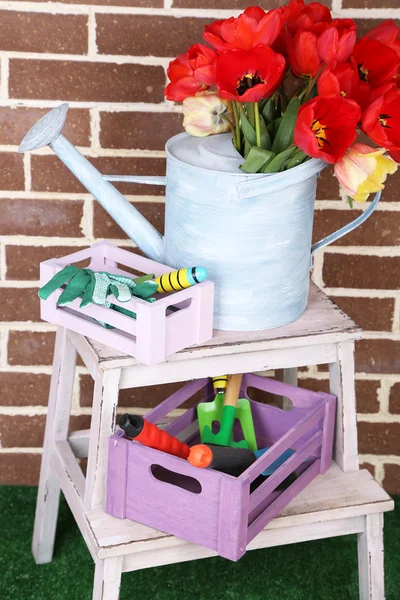 Composition of colorful tulips in watering can and equipment for gardening on bright background