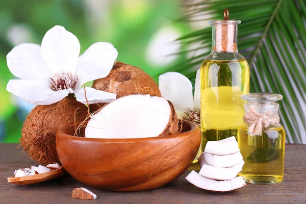 Coconuts and coconut oil on wooden table, on nature background