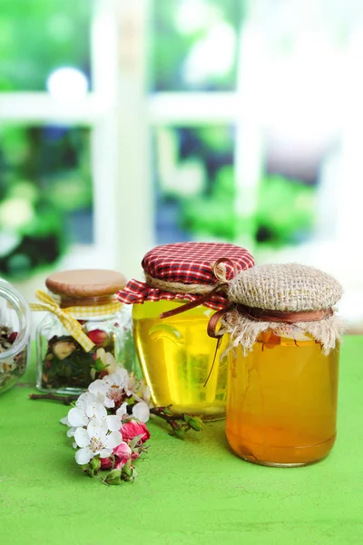 Assortment of herbs and tea and honey in glass jars on wooden table, on bright background