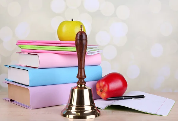 Gold school bell with school supplies on table on bright background