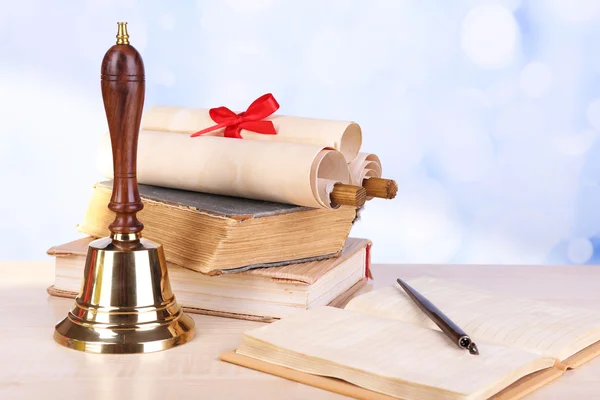 Gold school bell with school supplies on table on bright background