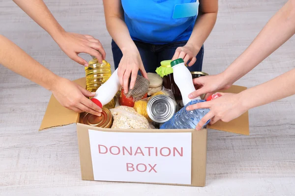 People makes foodstuffs out of donation box on grey background