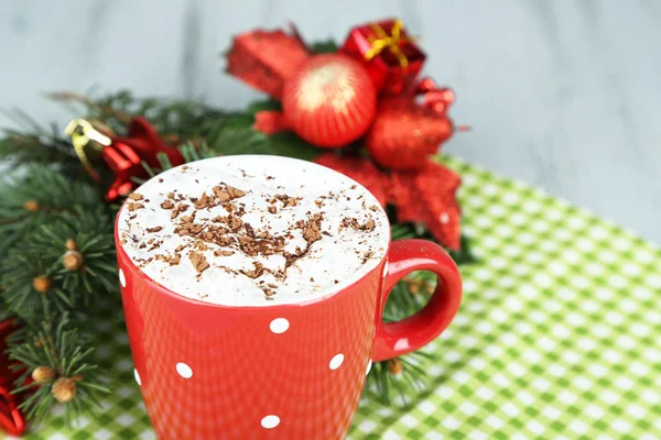 Hot chocolate with cream in color mug, on napkin, on Christmas decorations background