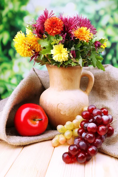 Composition with beautiful flowers in pitcher, and fruits,  on bright background