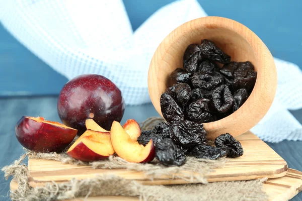 Fresh and dried plums in wooden bowl on napkin, on wooden background