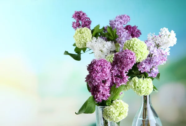 Beautiful spring flowers in glass bottles, on wooden table, on bright background