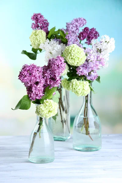 Beautiful spring flowers in glass bottles, on wooden table, on bright background