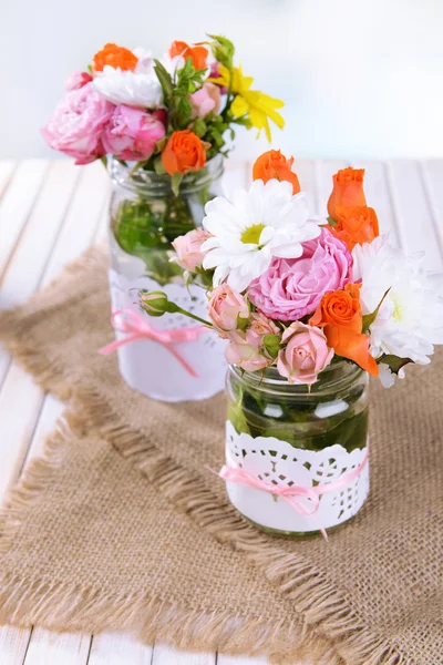 Beautiful bouquet of bright flowers in jars on table on light background