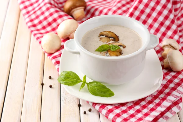 Mushroom soup in white pot, on napkin, on wooden background