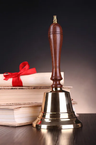 Gold retro school bell with books on table on dark background