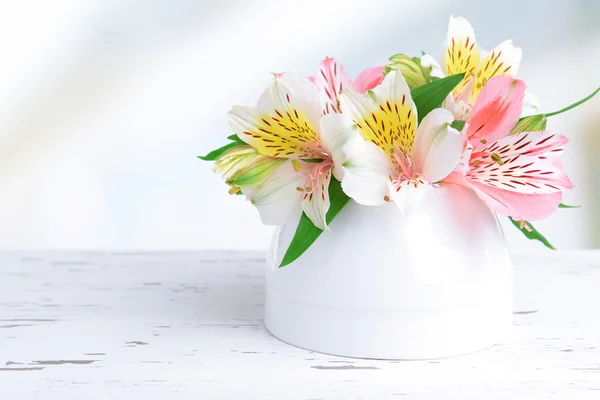 Alstroemeria flowers in vase on table on light background