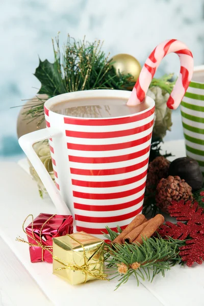 Cup of hot cacao with chocolates and Christmas decorations on table on bright background