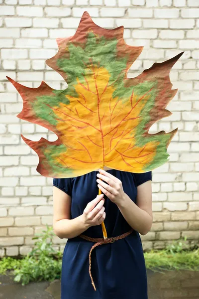 Girl holding decorative maple leaf on wall background