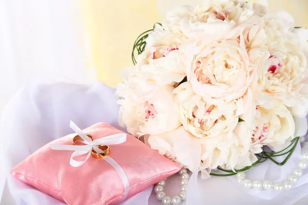 Beautiful wedding bouquet and decorative pillow for wedding rings on table on light background
