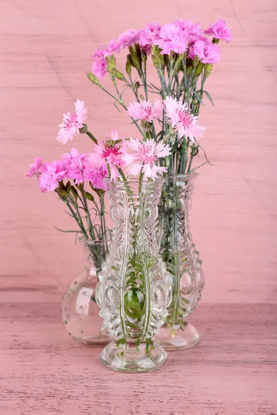Beautiful summer flowers in vases on pink wooden background