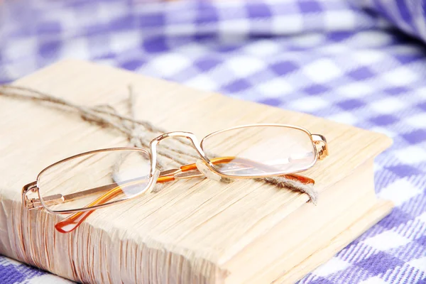 Composition with old book, eye glasses, and plaid on wooden background