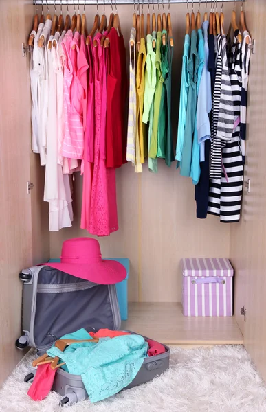 Female clothes in wardrobe and suitcase in room