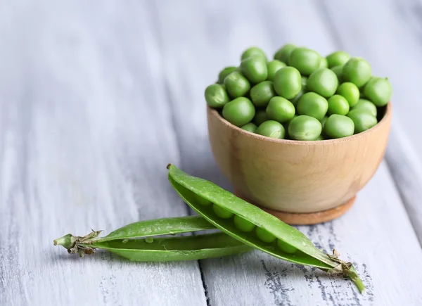 Green peas in wooden bowl on wooden background