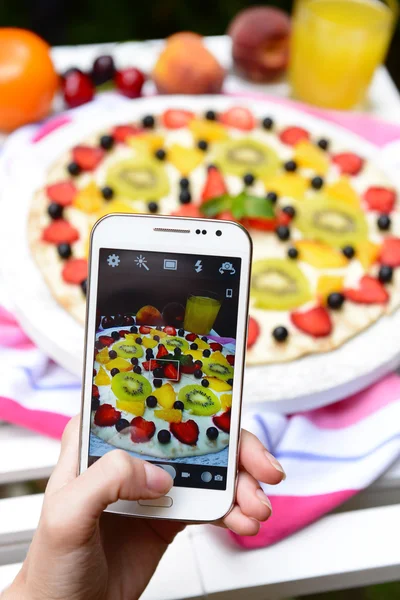 Hand making photo of fruit pizza on mobile phone for social network