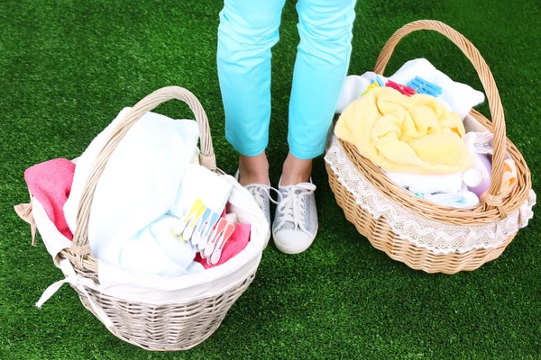 Woman holding laundry baskets with clean clothes, towels and pins, on green grass background