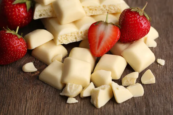 Broken white chocolate bar with fresh strawberries, on color wooden background