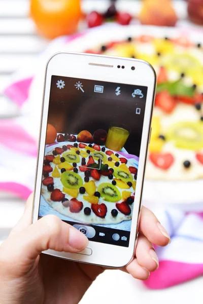 Hand making photo of fruit pizza on mobile phone