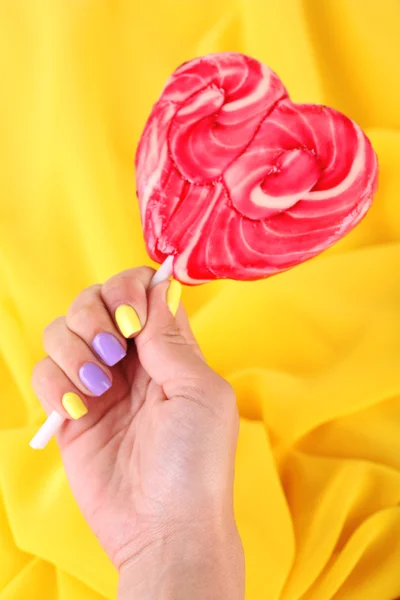Female hand with stylish colorful nails holding lollipop