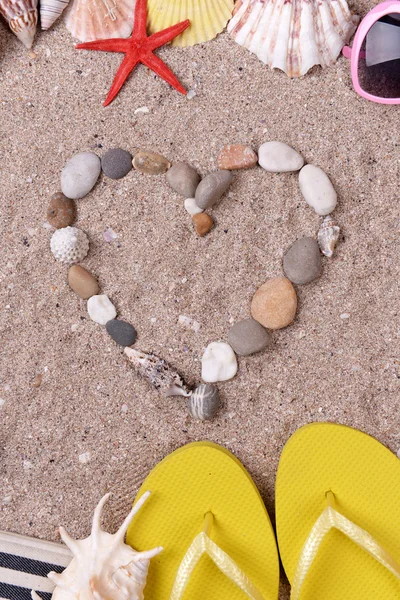 Shape of heart made from sea shells and stones on sand with beach accessories