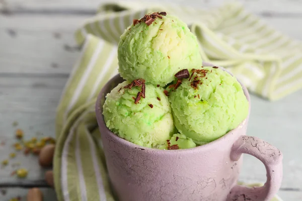 Tasty pistachio ice cream in cup on wooden table