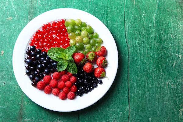 Forest berries on plate, on color wooden background