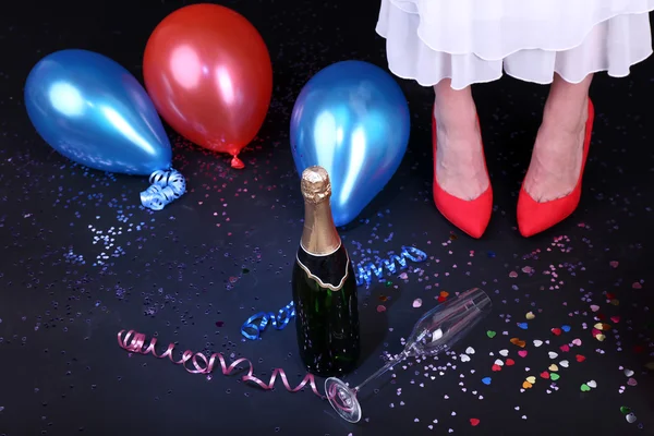 Legs with confetti, champagne and balloons on the floor