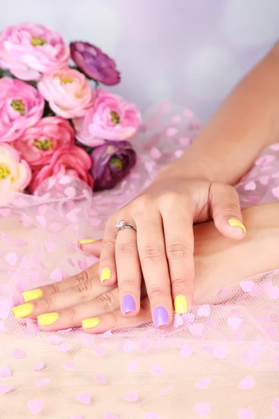 Female hand with stylish colorful nails, on color fabric background