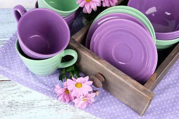 Bright dishes with flowers in crate on table close up