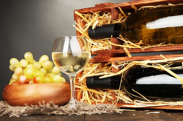 Wooden case with wine bottles, wineglass and grape on wooden table on grey background