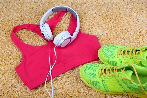 Sport clothes, shoes and headphones on color carpet background.