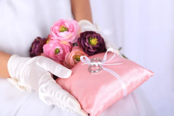 Bride in gloves holding wedding bouquet, and wedding rings close-up, on light background