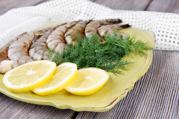 Square plate of prawns with dill and lemon on a yellow napkin on grey wooden background