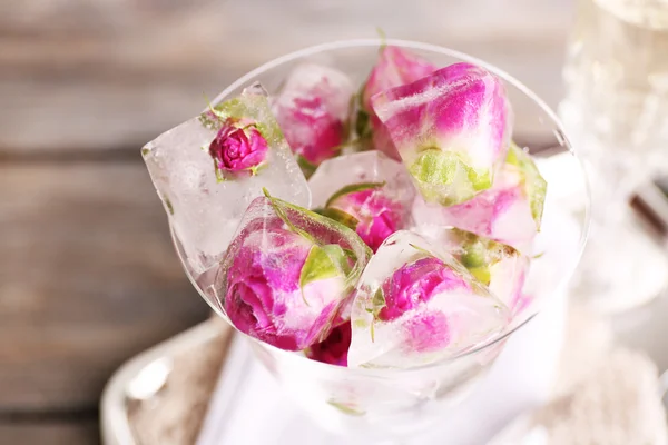 Ice cubes with rose flowers in glass bowl and two glasses with champagne on wooden table background