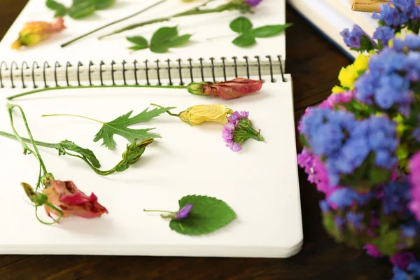 Composition with flowers and dry up plants on notebook on table close up