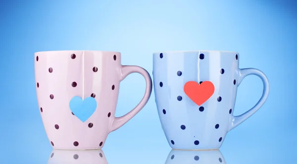 Two cups and tea bags with red and blue heart-shaped label on blue backgrou