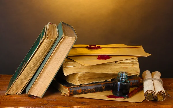 Old books, scrolls, ink pen and inkwell on wooden table on brown background