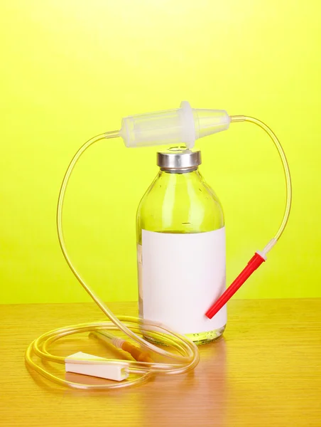 Bottle of intravenous antibiotics and plastic infusion set on wooden table on green background