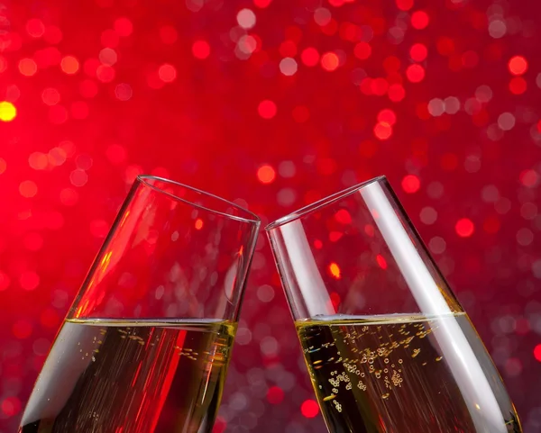 Champagne flutes with gold bubbles on red light bokeh background