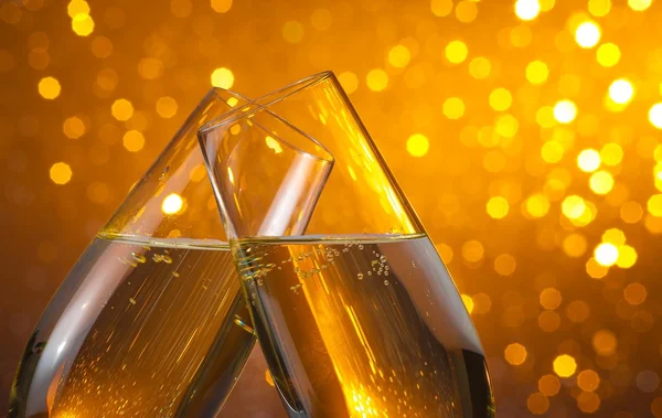 Two champagne flutes with gold bubbles on dark light bokeh background