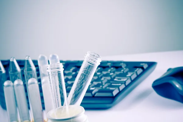 Test tubes in laboratory on table near computer keyboard and mouse — Stock Photo #37929707
