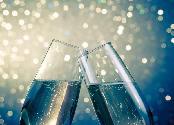 Champagne flutes with golden bubbles on blue light bokeh background