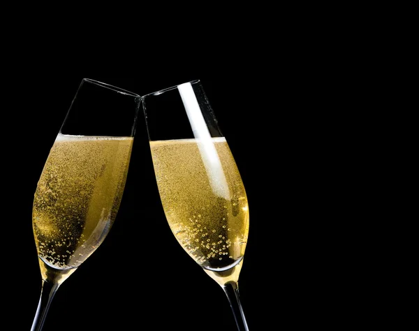 Two champagne flutes with golden bubbles make cheers on black background